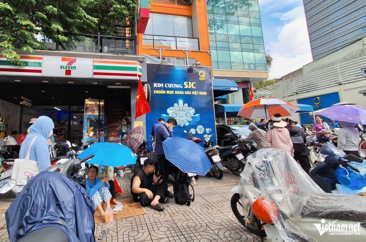 Khách hàng trải bạt trên vỉa hè, cầm ô chờ đến lượt mua vàng. Có người cho hay đã phải xếp hàng mua vàng từ 10h tối hôm trước.